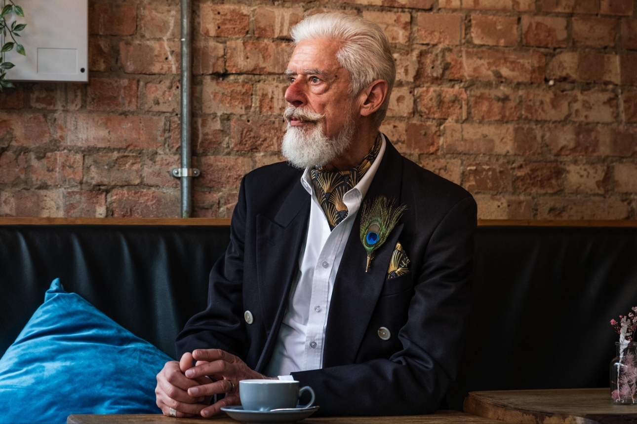 older gent sat down with peacock themed accessories